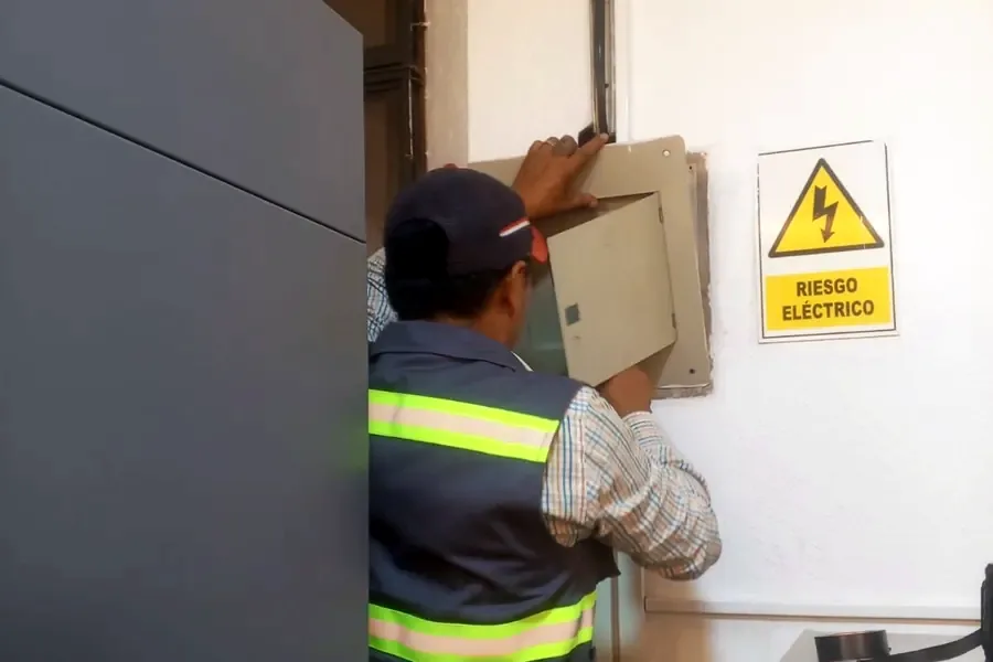 Electricista con casco de seguridad junto a un medidor eléctrico