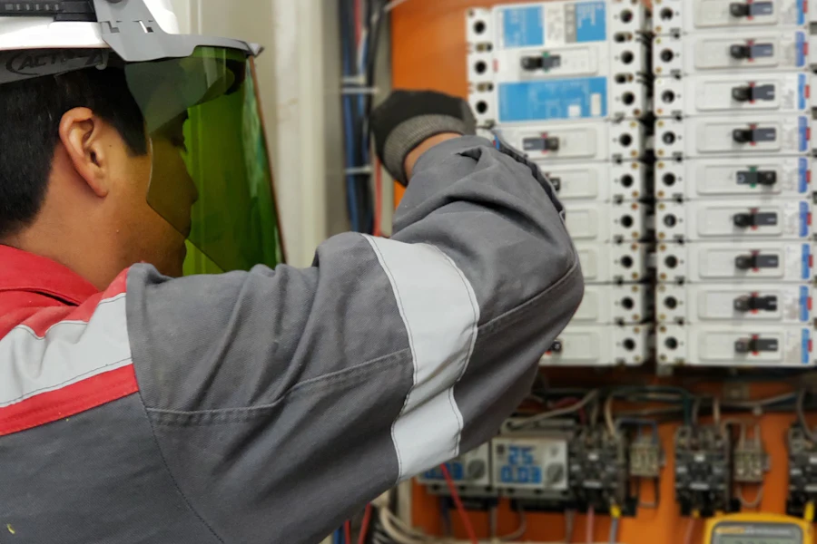 Técnico con careta de protección revisando un tablero de breakers